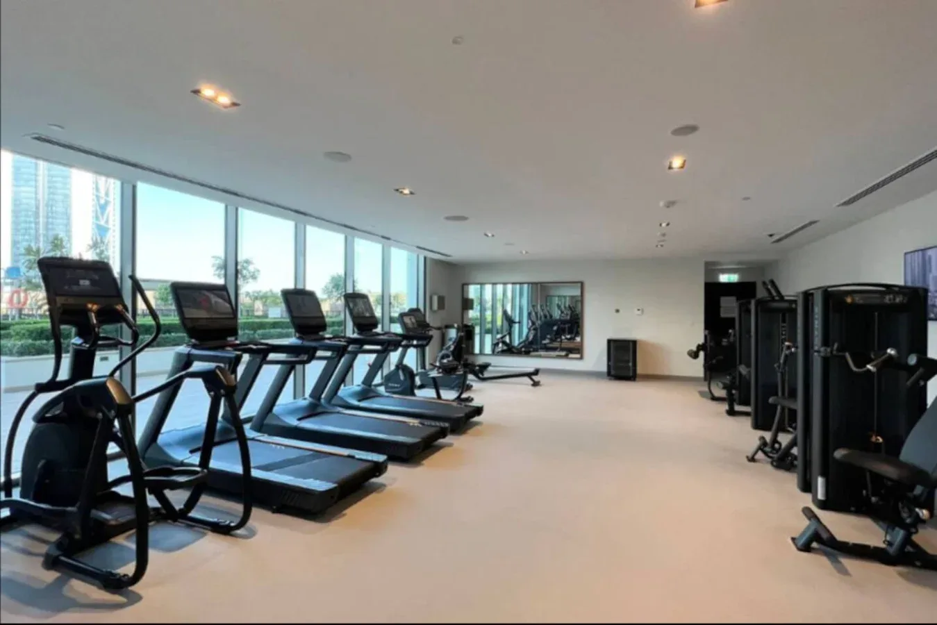 Un gimnasio luminoso con máquinas de ejercicio junto a grandes ventanales.