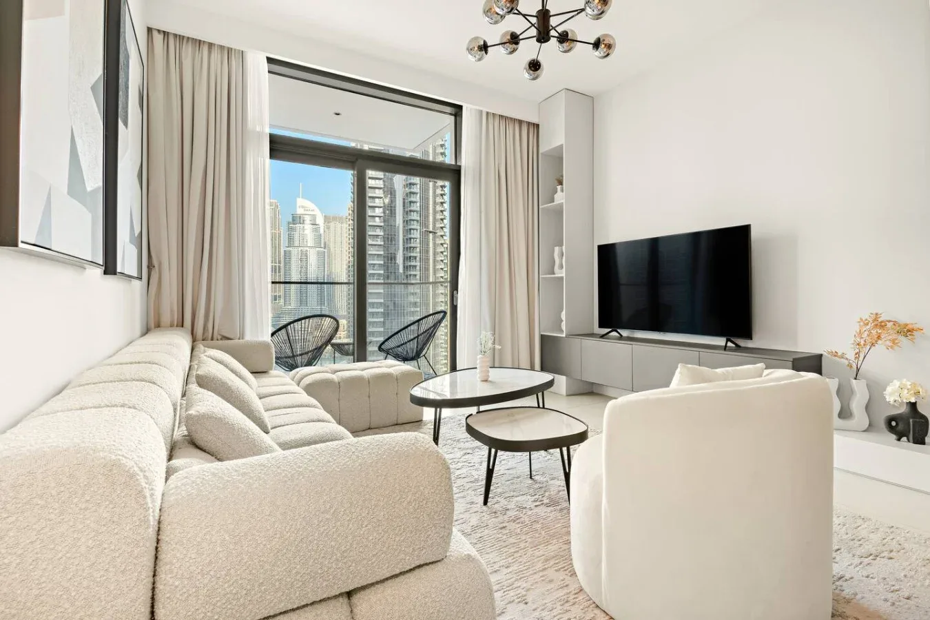 Una sala luminosa con asientos, un televisor y grandes ventanas con vistas a edificios cercanos.