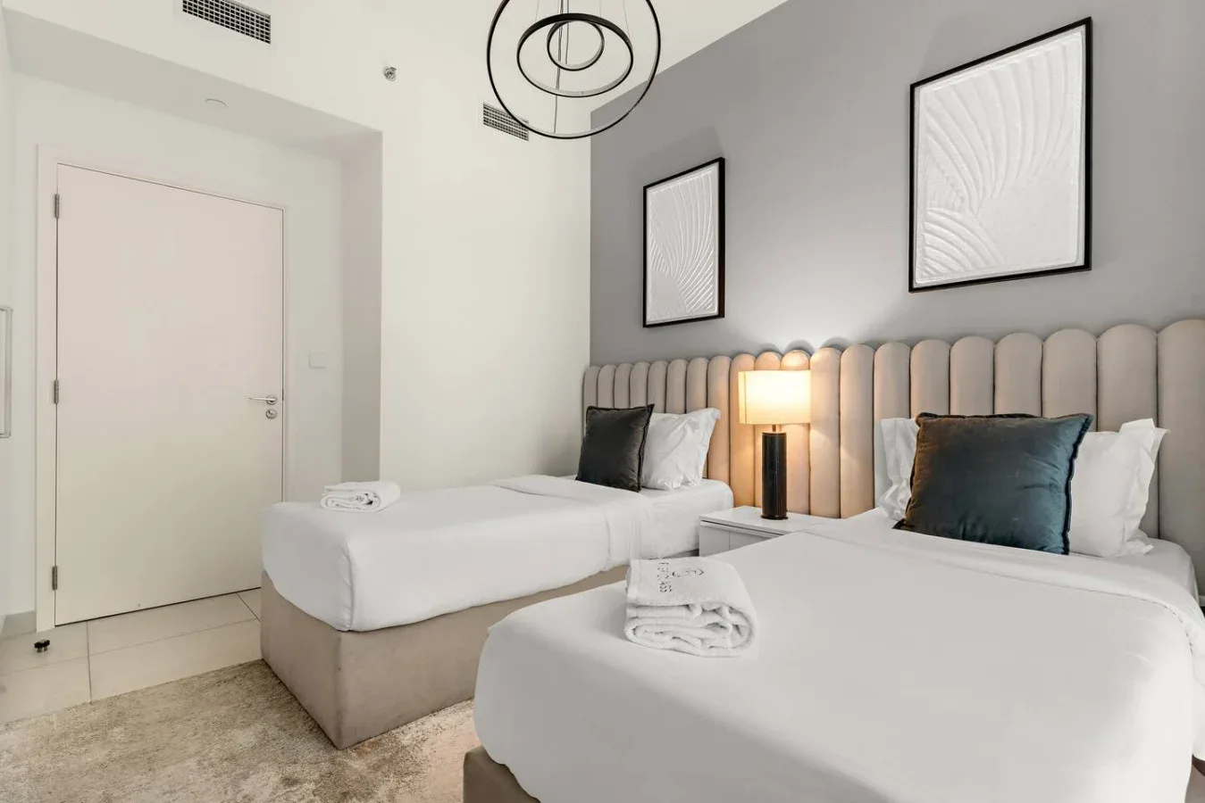 Un dormitorio luminoso con dos camas bien arregladas y cuadros enmarcados.