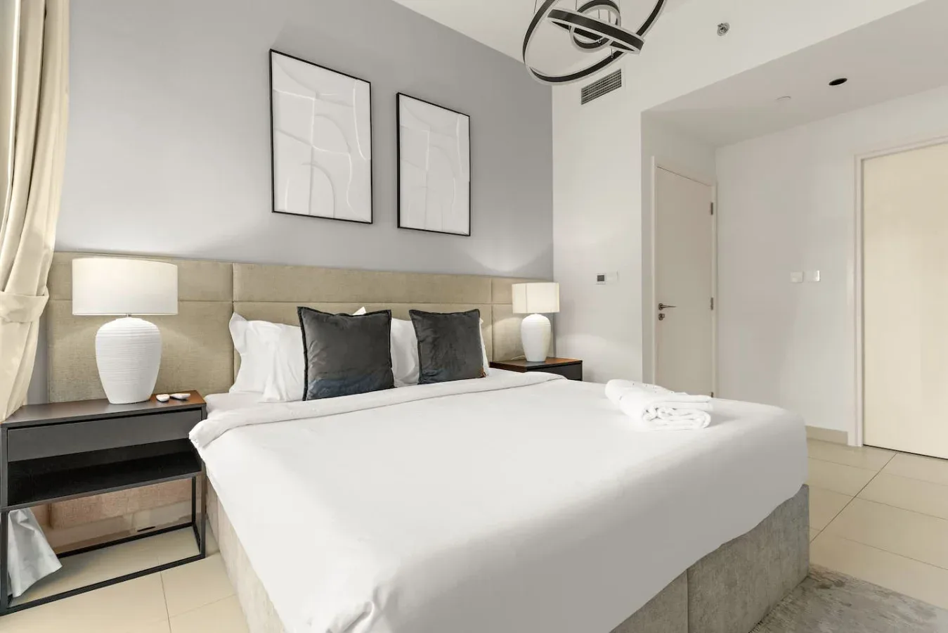 Un dormitorio con una cama bien tendida, cojines oscuros y cuadros en la pared.