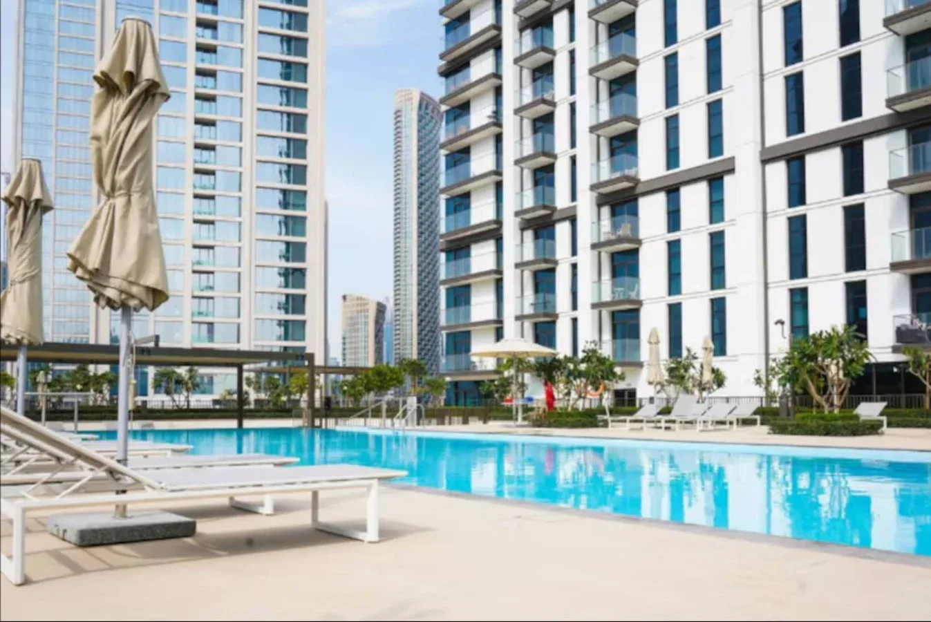 Una piscina al aire libre está junto a edificios altos modernos y asientos de descanso.
