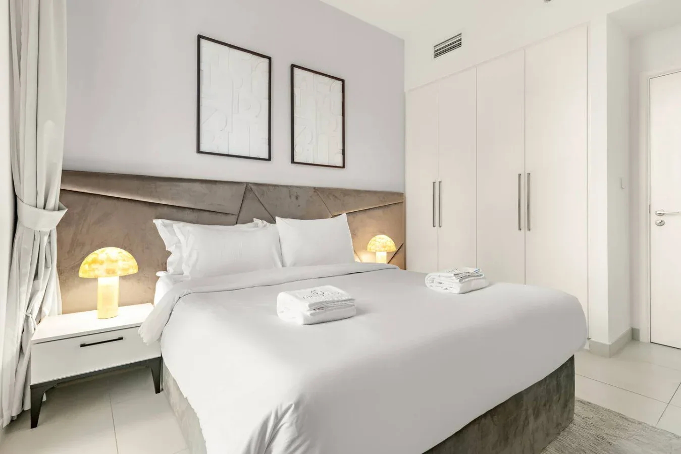 Un dormitorio luminoso con una cama bien hecha y armarios blancos.