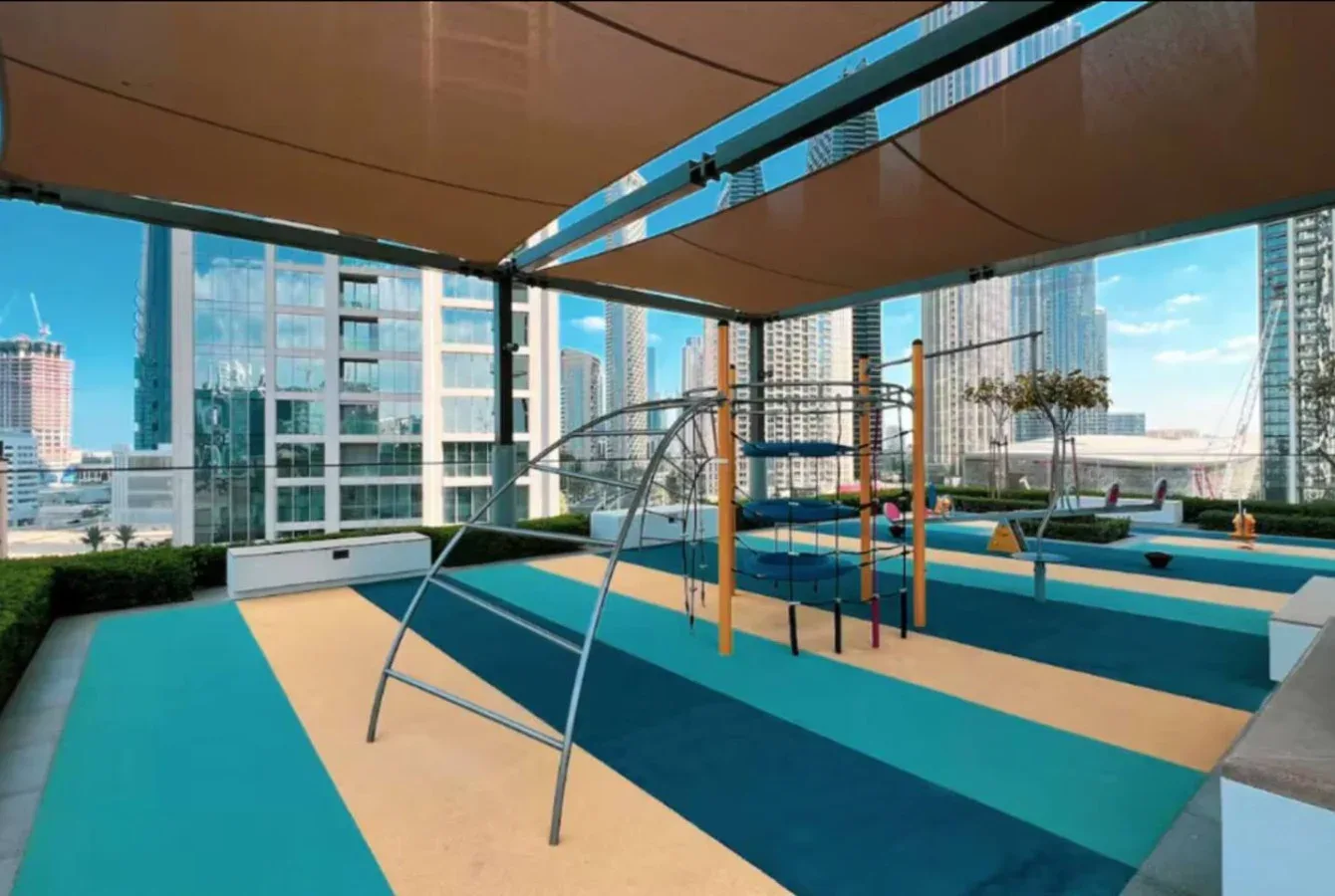 Una zona de juegos en la azotea, con suelo de colores y estructuras para trepar, ofrece vistas de la ciudad.
