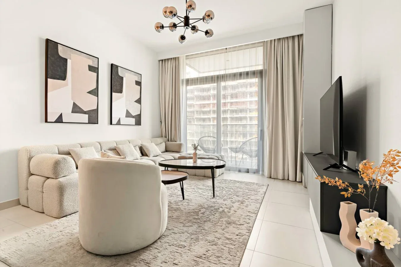 Una sala luminosa con asientos neutros, una mesa de centro y grandes ventanas con cortinas.