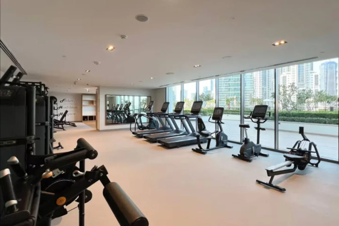 Una sala de ejercicio con máquinas y cintas de correr junto a grandes ventanales.