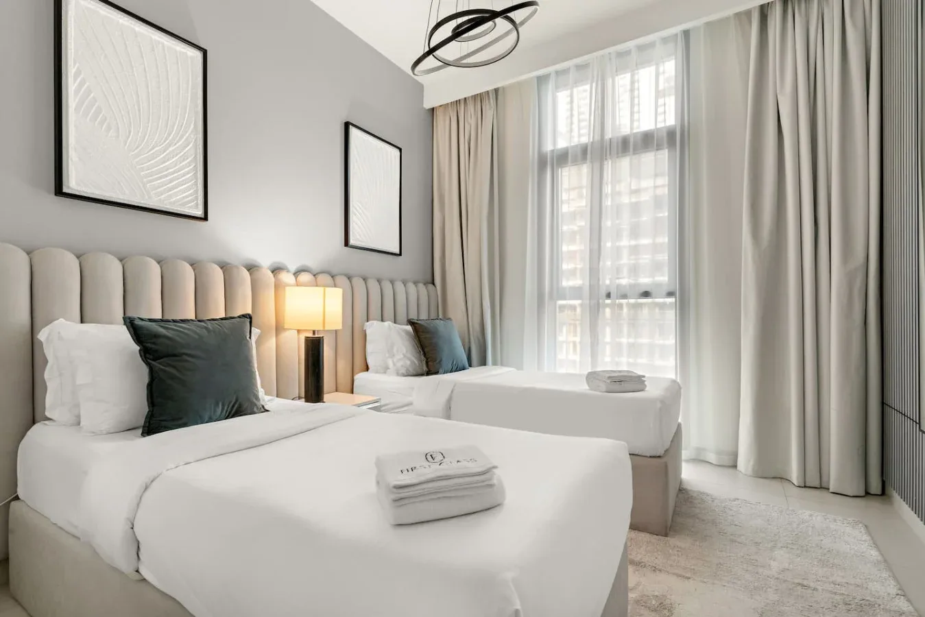Un dormitorio luminoso con dos camas junto a una gran ventana con cortinas.