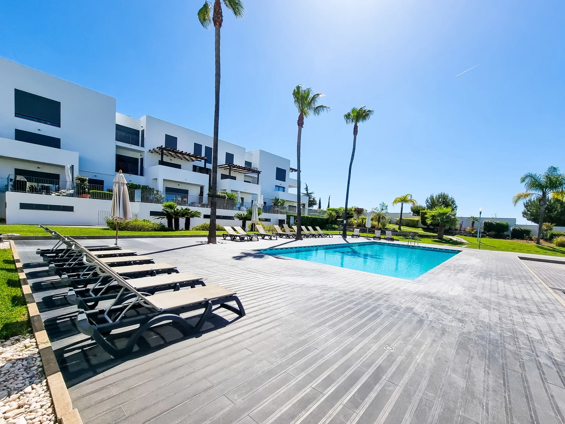 Una piscina al aire libre y su terraza están junto a una hilera de apartamentos modernos.