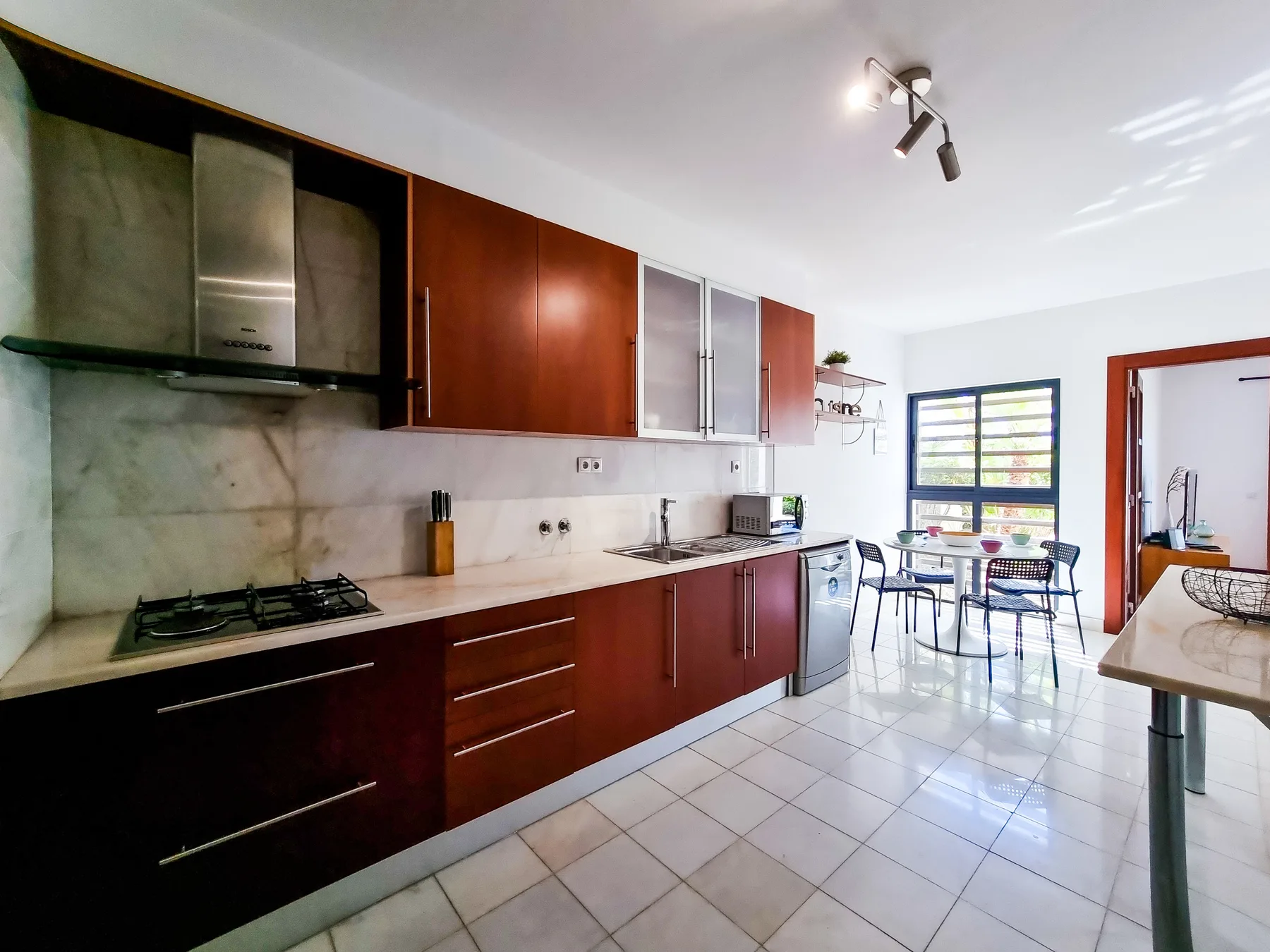 Una cocina moderna con gabinetes de madera oscura y un pequeño comedor junto a la ventana.