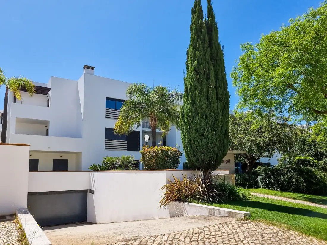 Un edificio blanco moderno se encuentra junto a una entrada pavimentada y un jardín ajardinado.