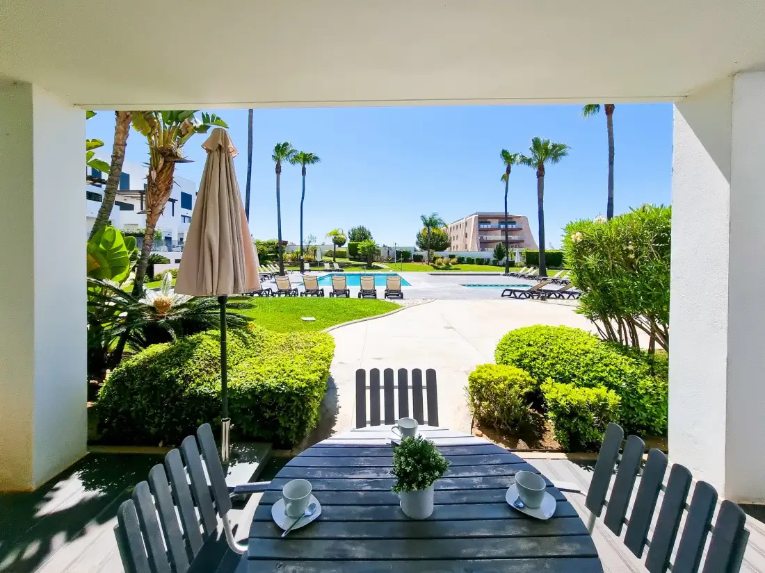 Un patio sombreado con asientos al aire libre da a una zona de piscina ajardinada.