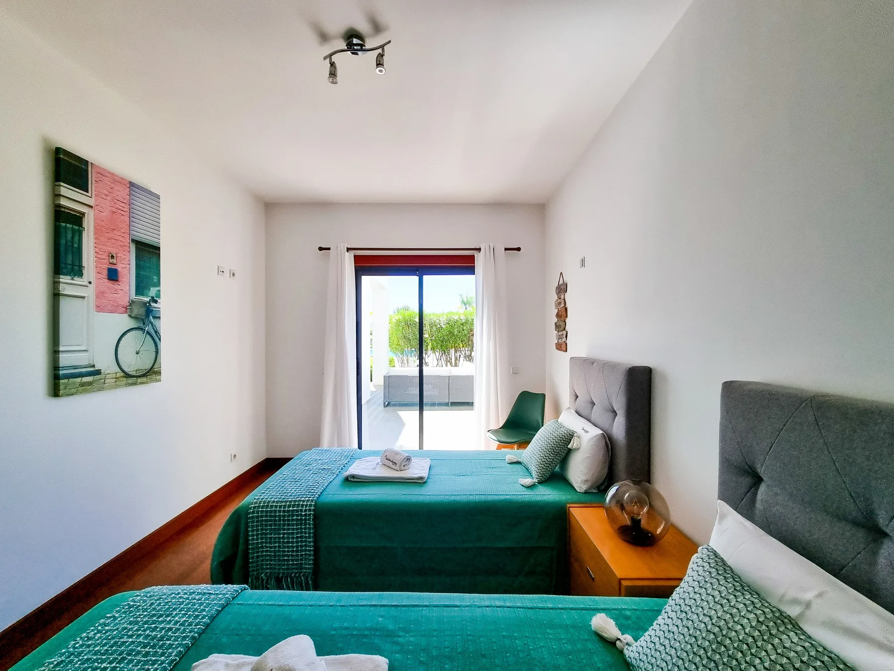 Un dormitorio luminoso con dos camas y puertas correderas de cristal que dan a un balcón.