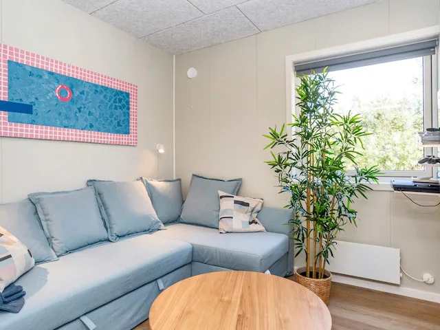 Una sala de estar con asientos azul claro, una mesa redonda de madera y una ventana grande.