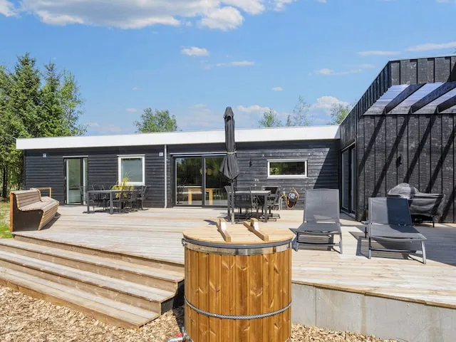 Una casa vacacional moderna da a una amplia terraza con asientos al aire libre y una bañera de hidromasaje de madera.