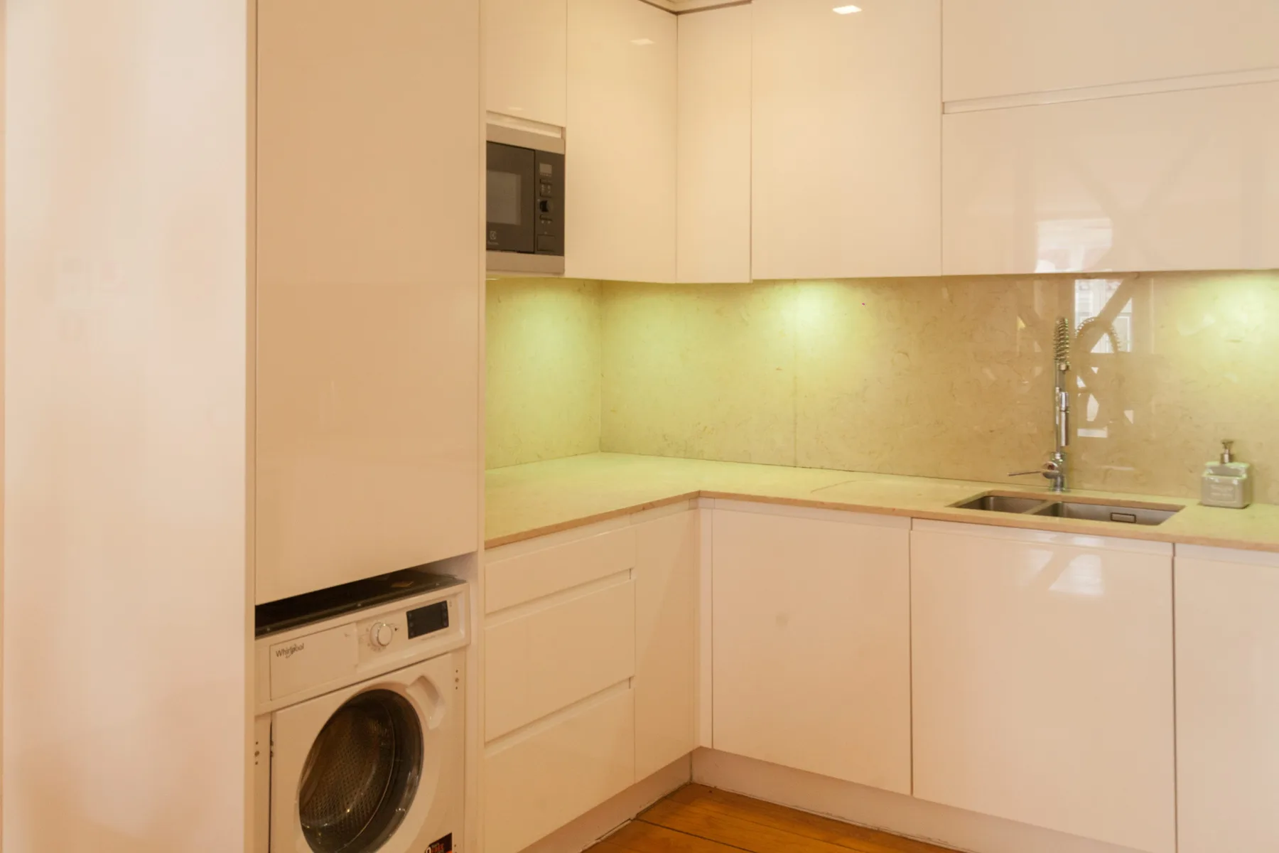 A compact kitchen with pale cabinets, a sink, and a washing machine.