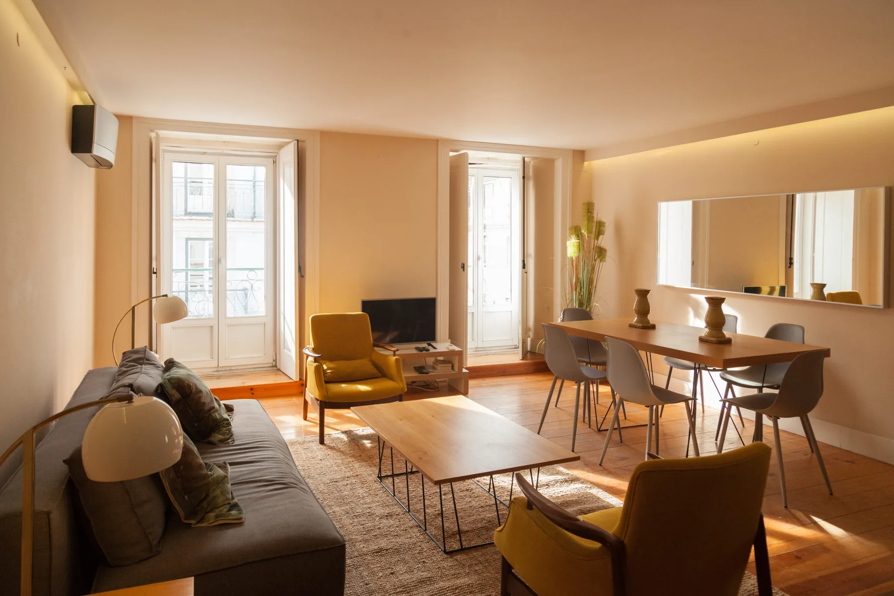 A warm living and dining area with seating, a coffee table, and tall windows.