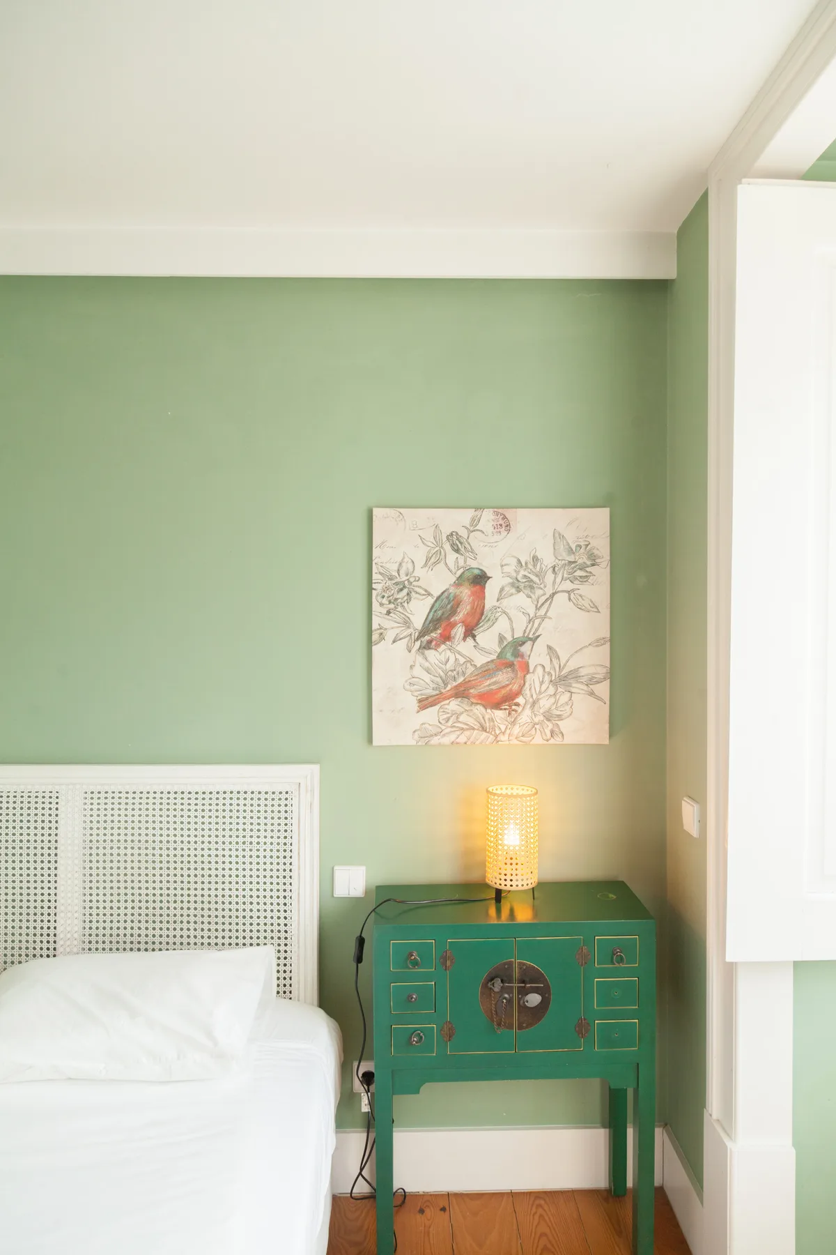 A bedroom with a green bedside table and a bird illustration on the wall.