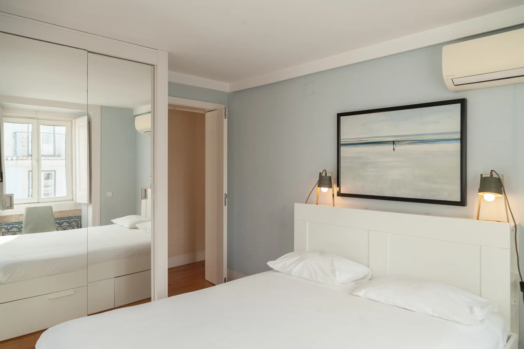 Bedroom with a bed, mirrored wardrobe, and framed artwork above the headboard.