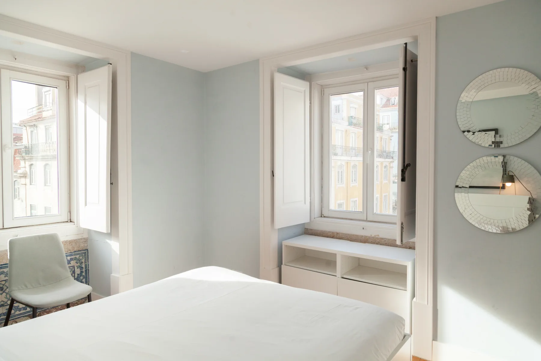 A bright bedroom with a bed, two windows, and a built-in window seat.