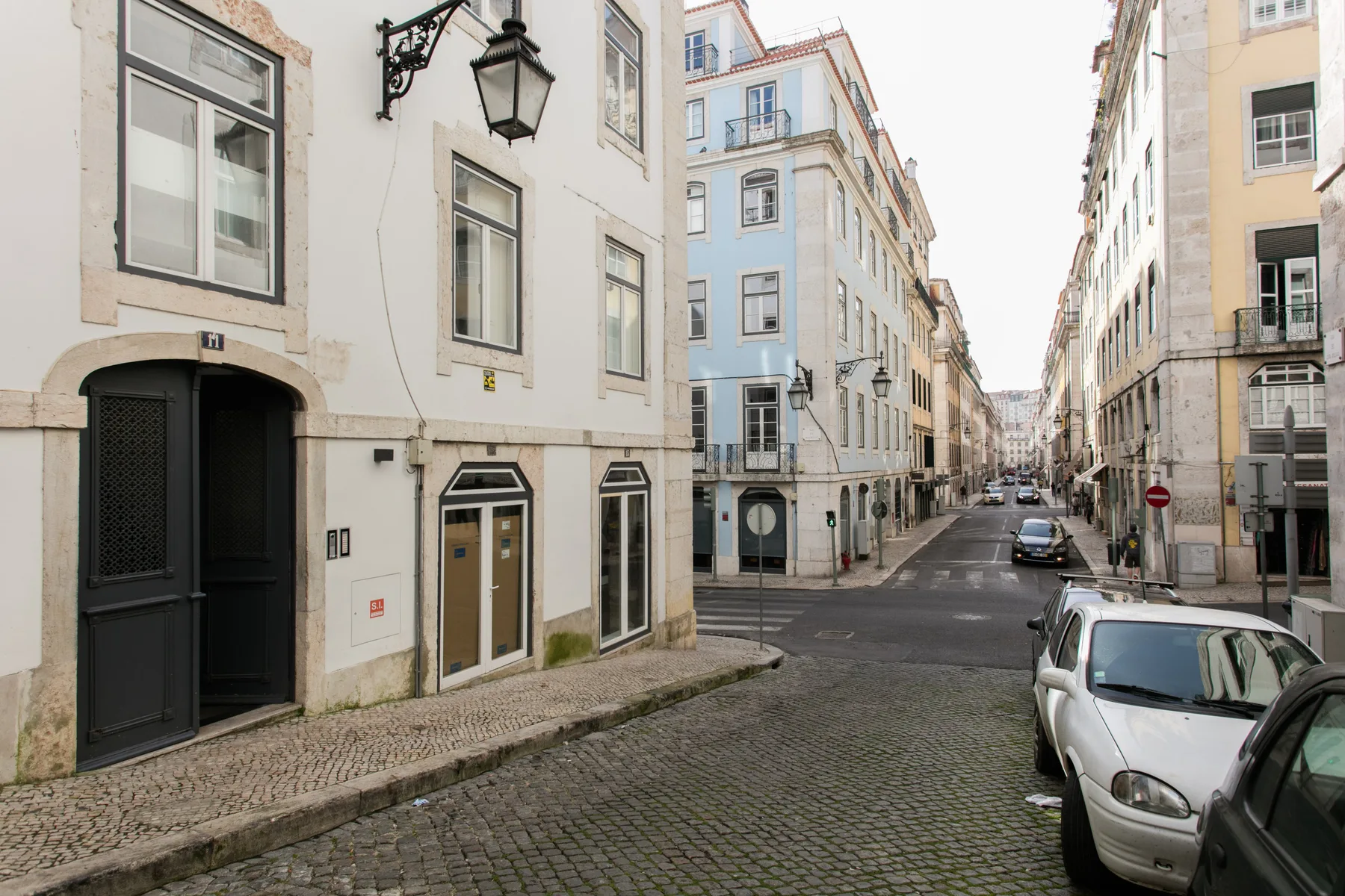 A cobbled city street lined with multistory buildings and parked cars.