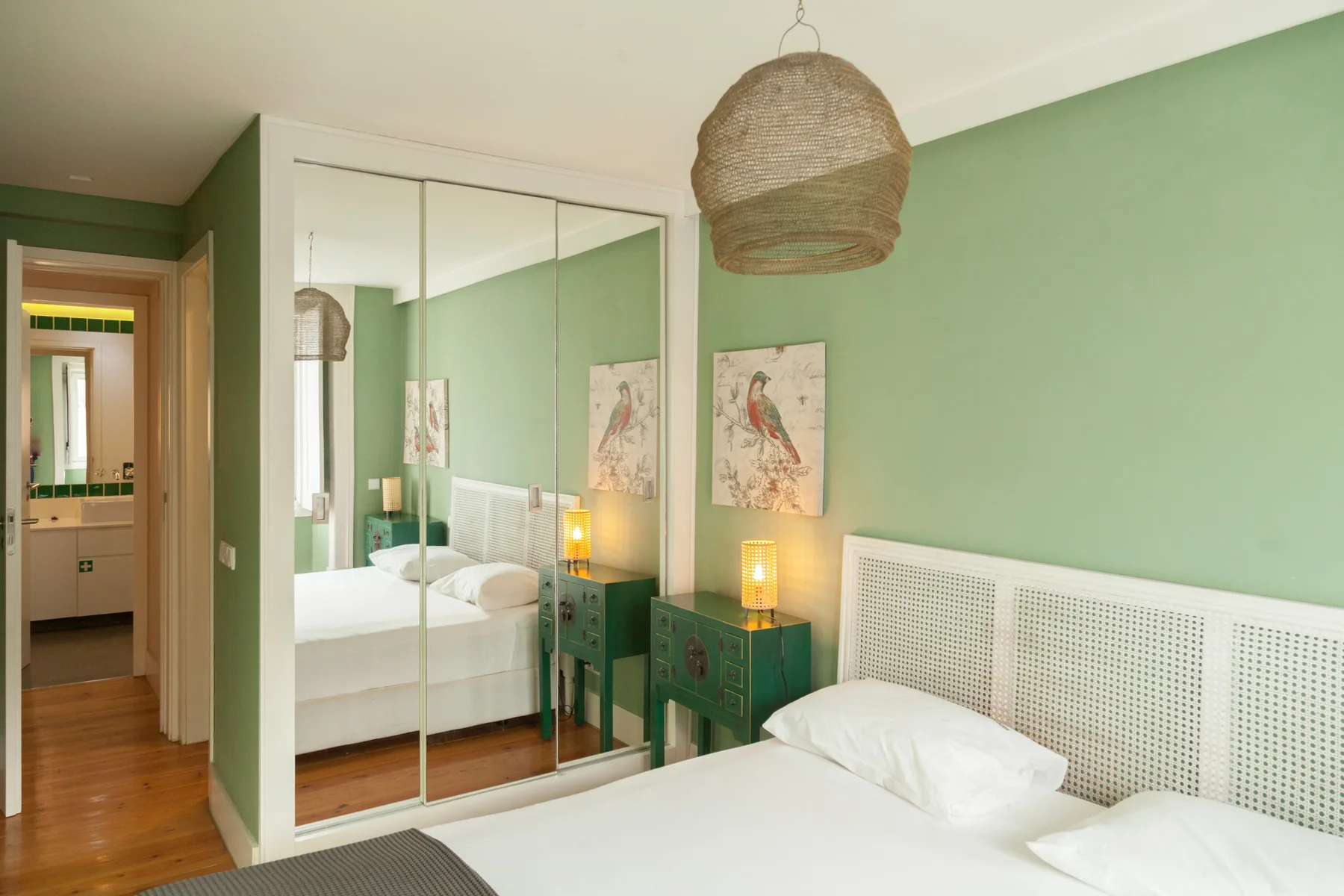 A bedroom with a bed, mirrored wardrobe, and green walls.