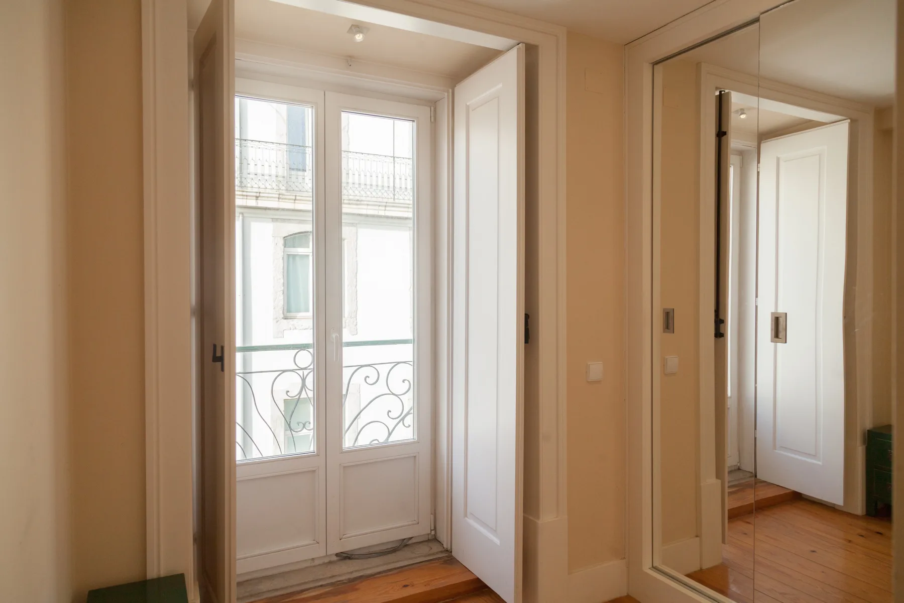 A bright interior doorway opens onto tall glazed doors, with a mirrored closet nearby.