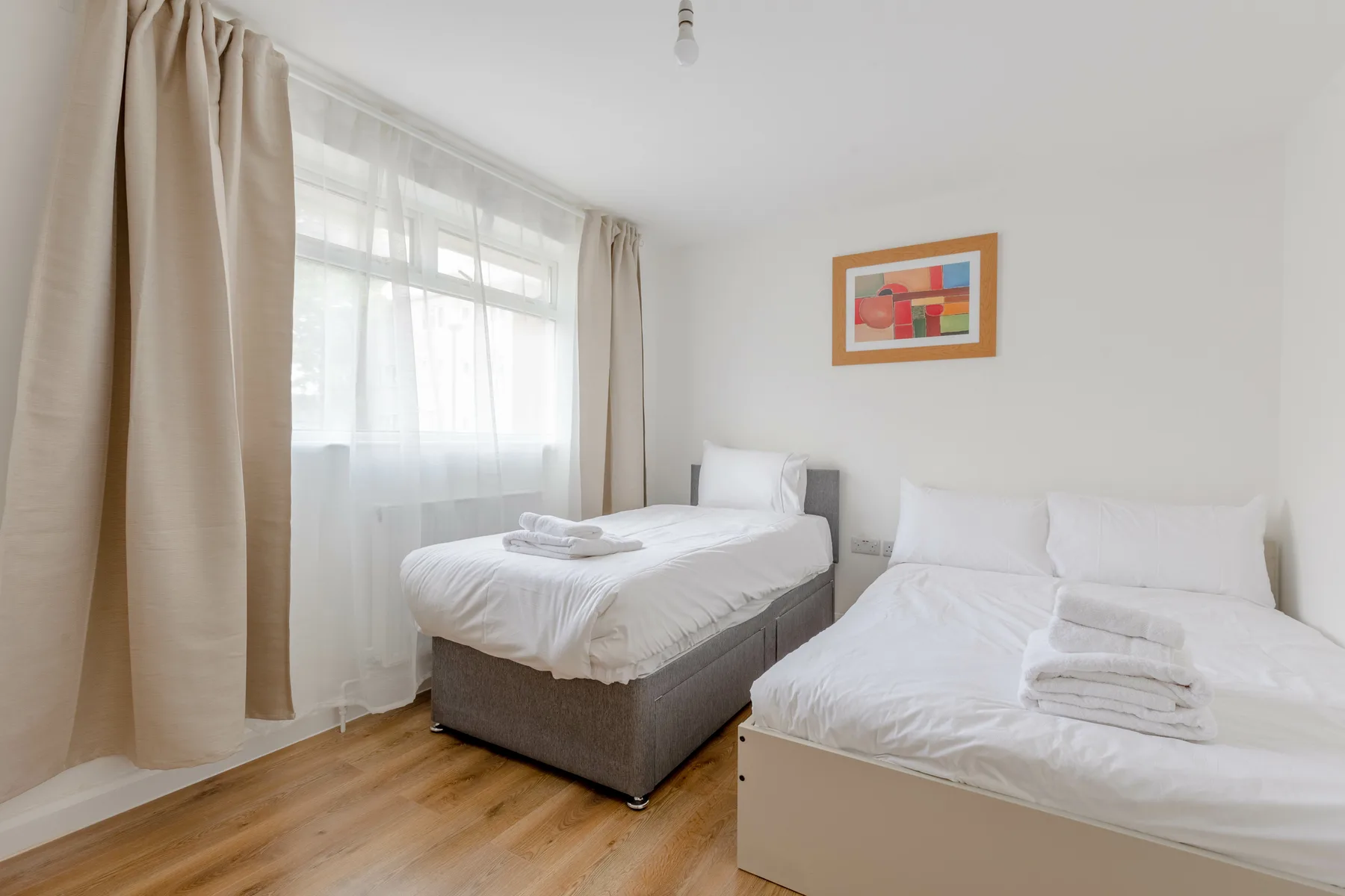 A bright bedroom with two beds beside a curtained window.