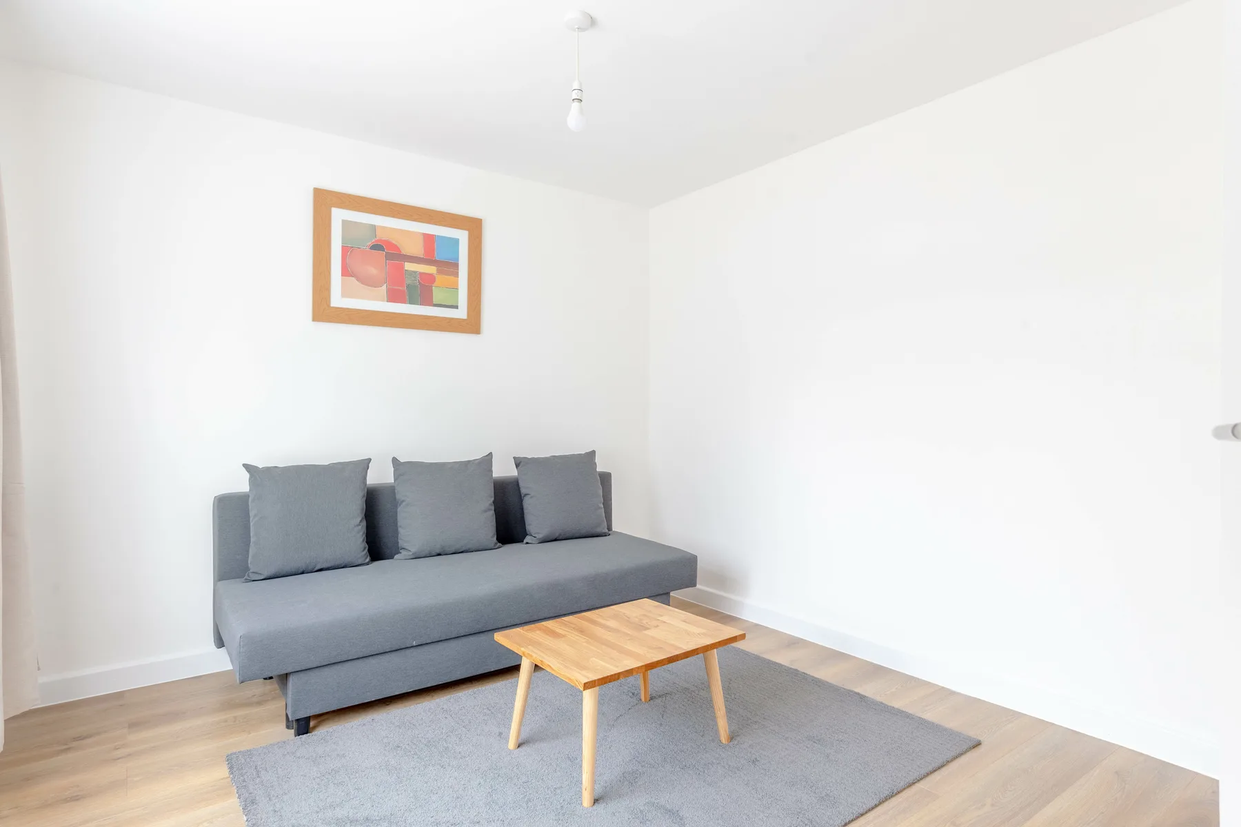 Sala luminosa con asientos grises, una mesa de centro de madera y un cuadro enmarcado.