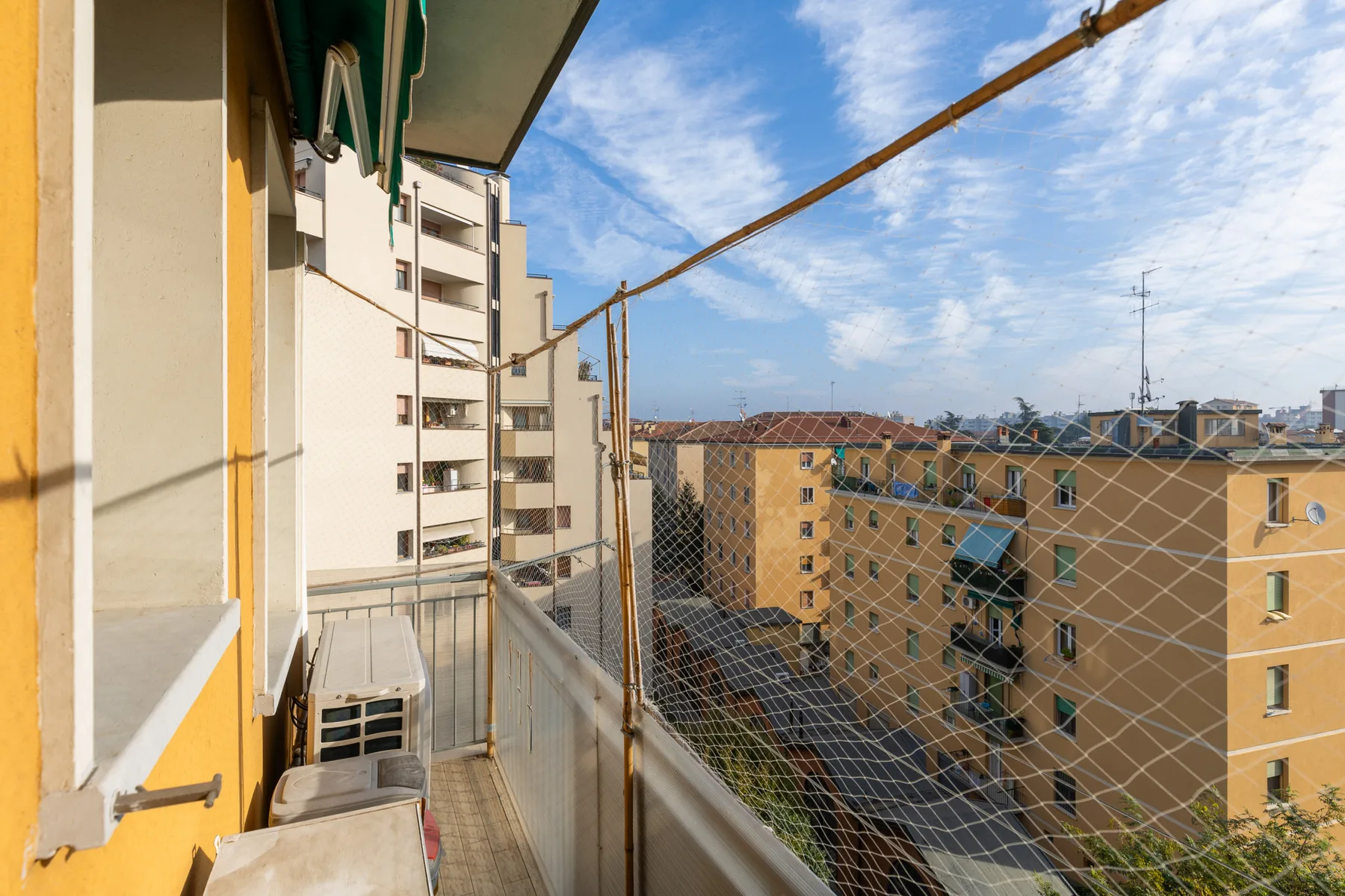 Un balcón estrecho da a edificios de apartamentos bajo un cielo azul.
