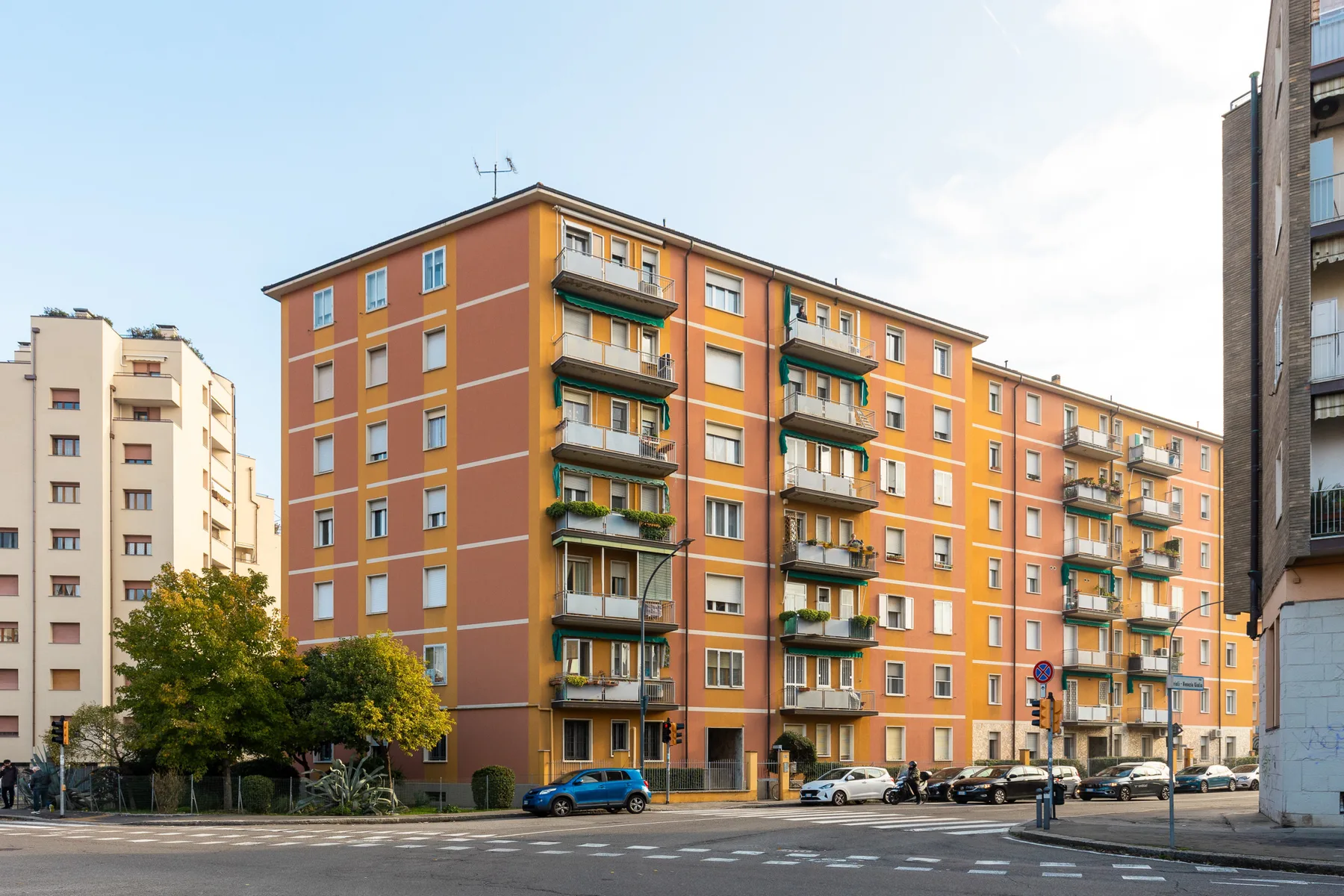 Un edificio de apartamentos naranja con balcones se alza junto a una calle urbana.
