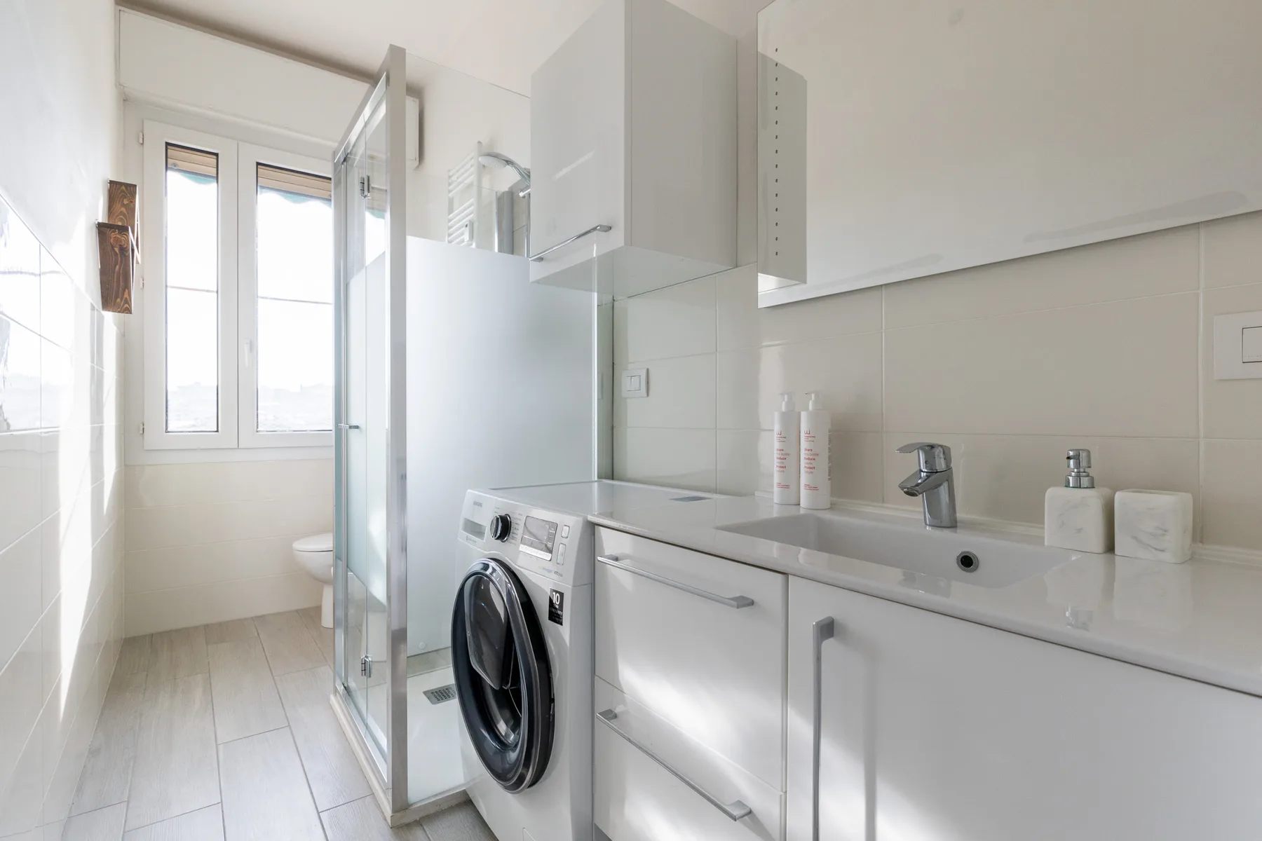 Un baño luminoso con ducha de vidrio, lavadora y lavabo.