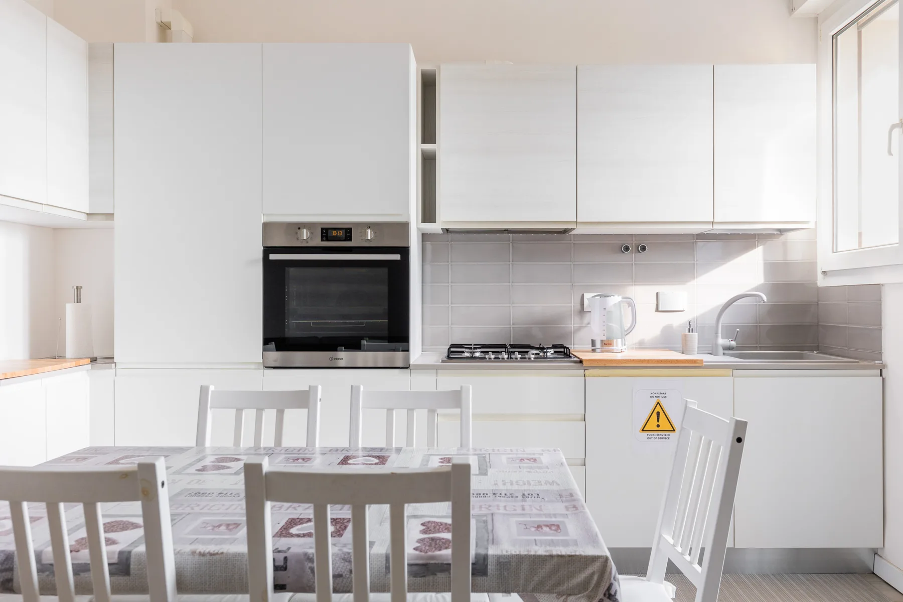 Una cocina luminosa con armarios blancos, una cocina y una mesa de comedor.