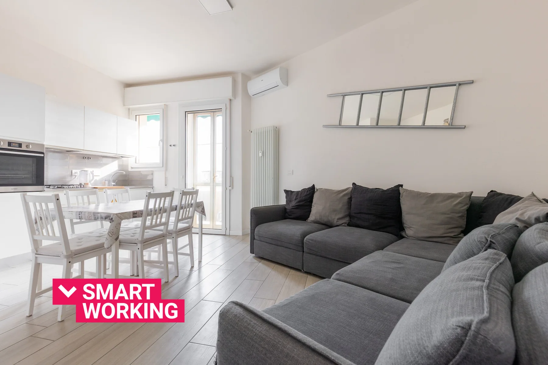 A bright living room with a sectional sofa, dining table, and kitchen.