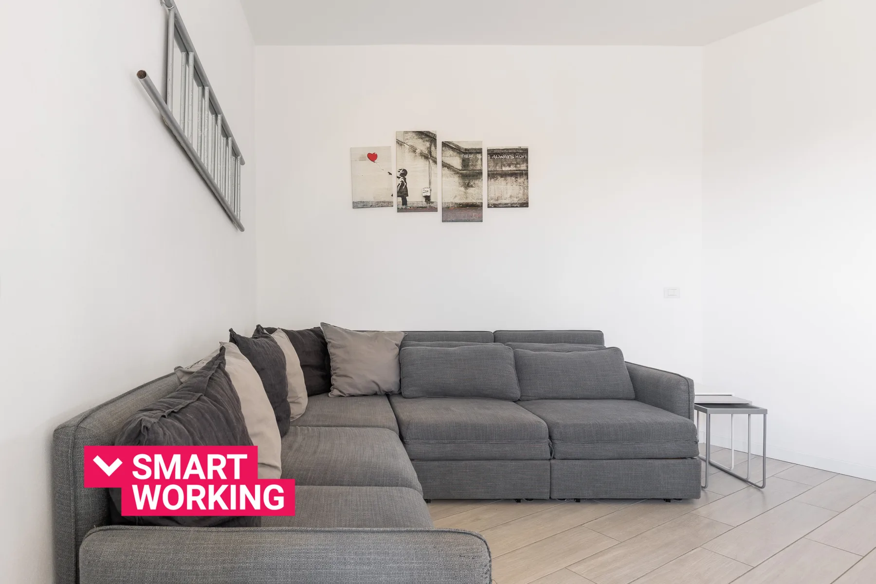Una sala luminosa con un sofá seccional gris y cuadros en la pared.