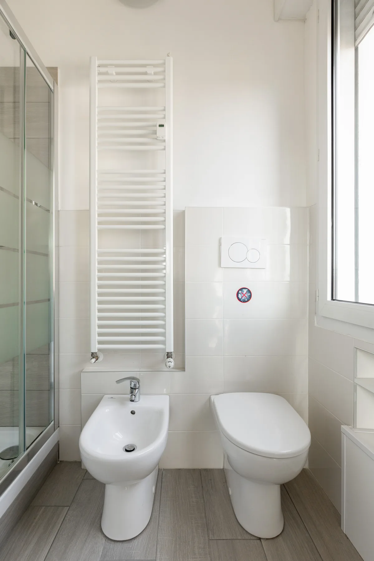 Un baño luminoso con bidé, inodoro y ducha de vidrio.