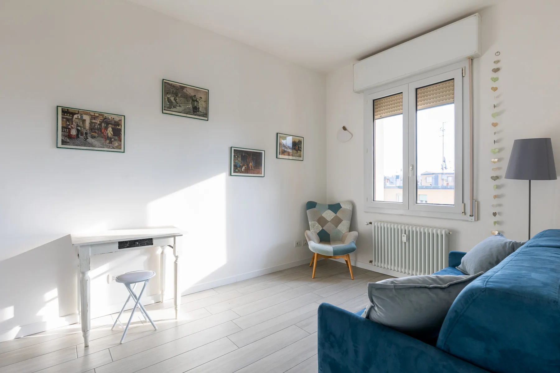 Una sala luminosa con un sofá azul, un escritorio pequeño y una ventana.