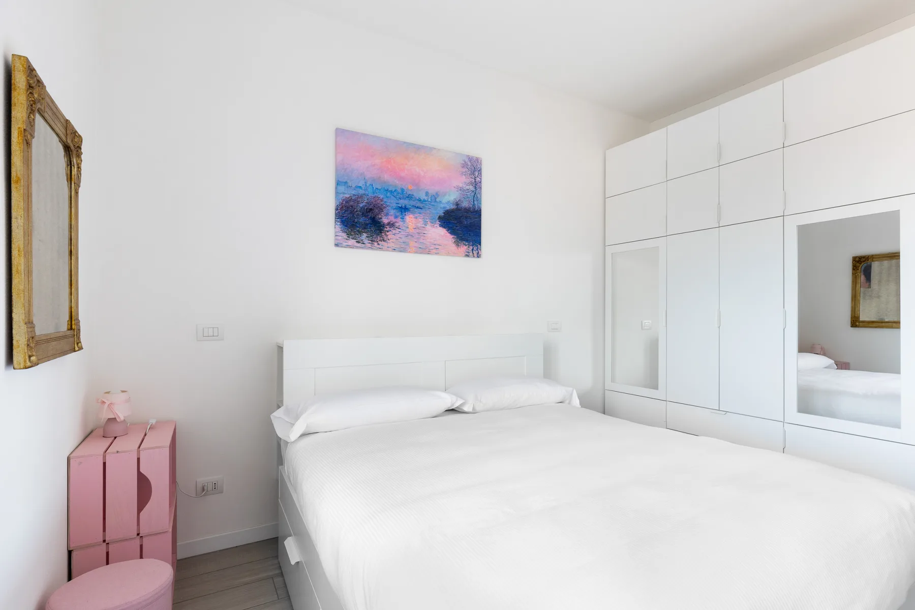Un dormitorio luminoso con ropa de cama blanca y un cuadro colorido sobre la cama.