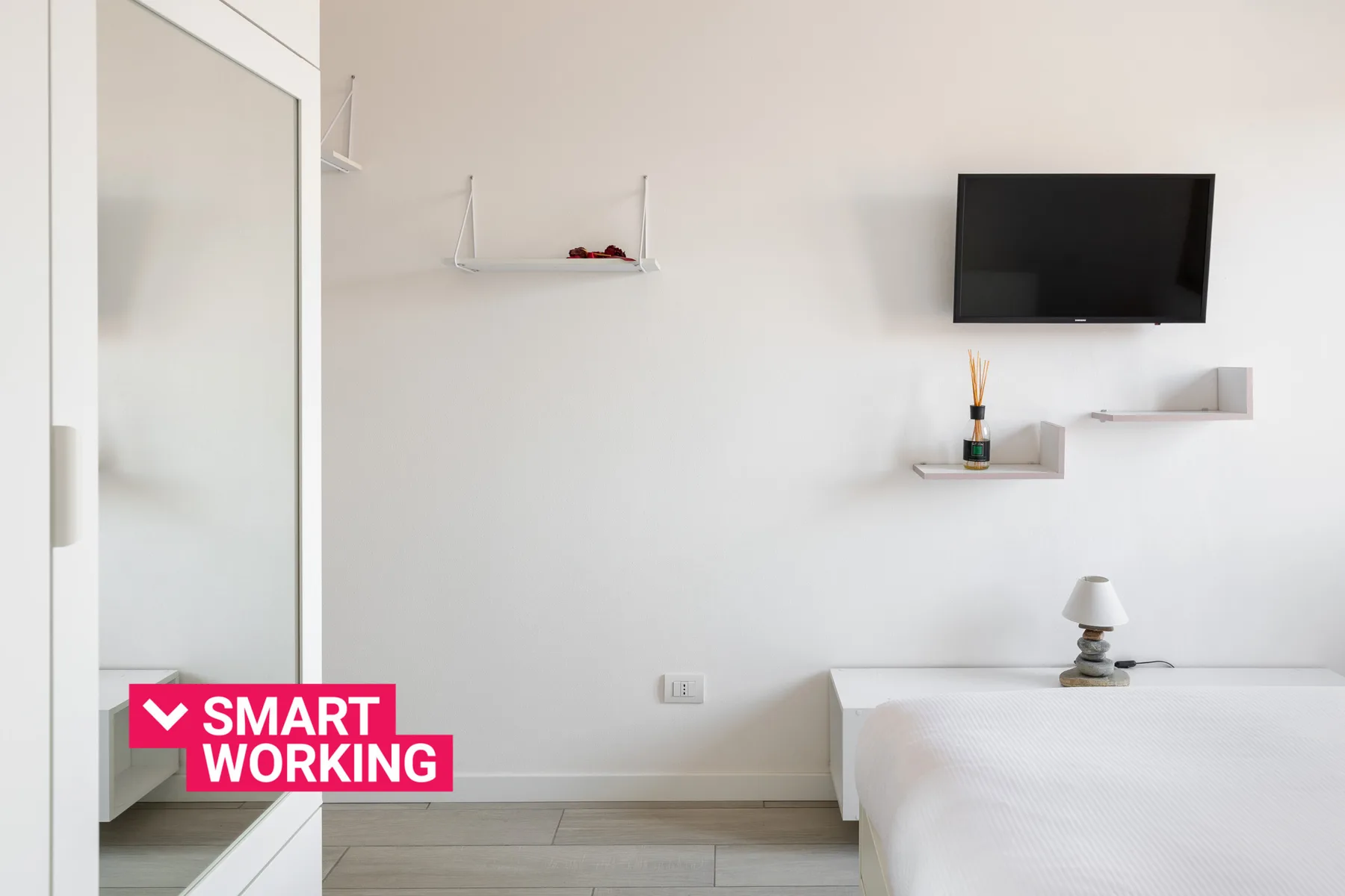 Un dormitorio luminoso con una cama, un televisor en la pared y estantes flotantes.
