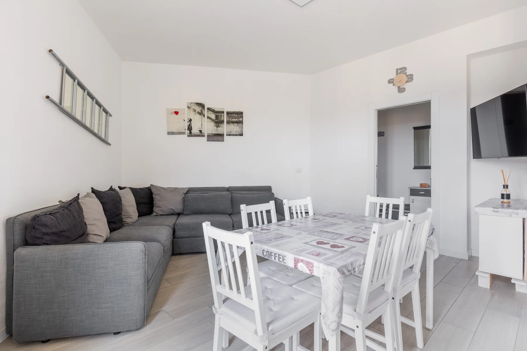 Una sala de estar y comedor con un sofá seccional gris y una mesa blanca.