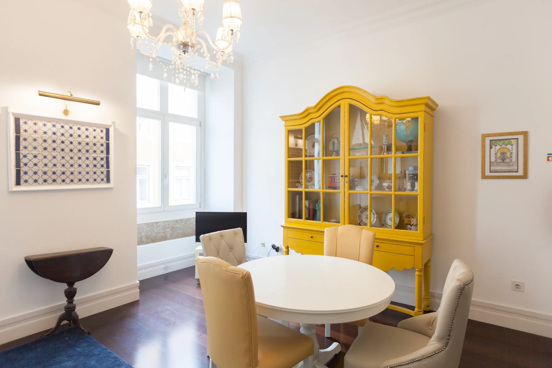 Comedor con una mesa redonda y un armario amarillo con puertas de cristal.