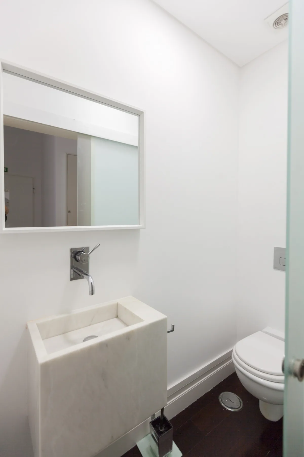 Un baño luminoso con lavabo suspendido, espejo e inodoro.