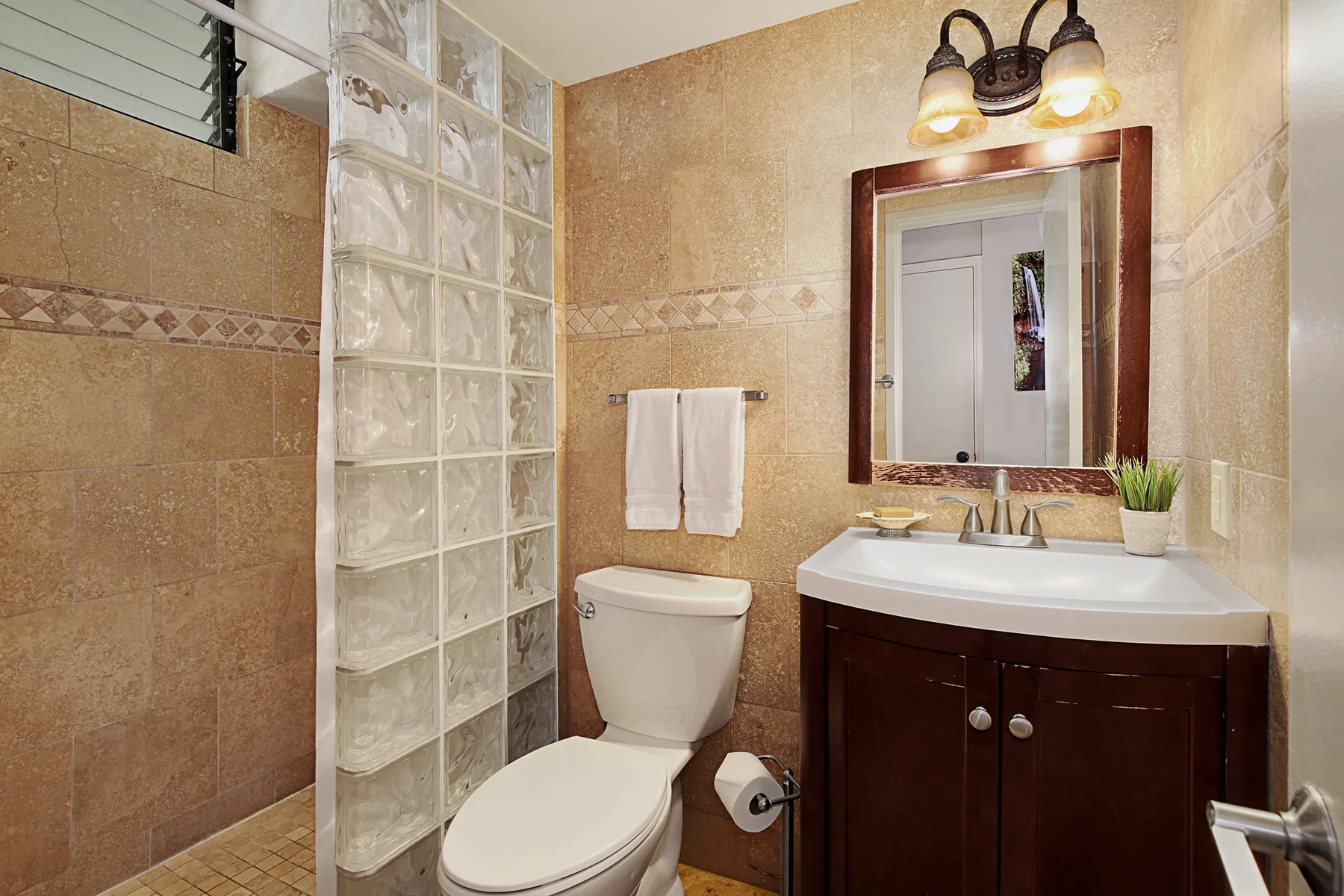 Un baño alicatado con inodoro, separador de bloques de vidrio y lavabo con mueble.