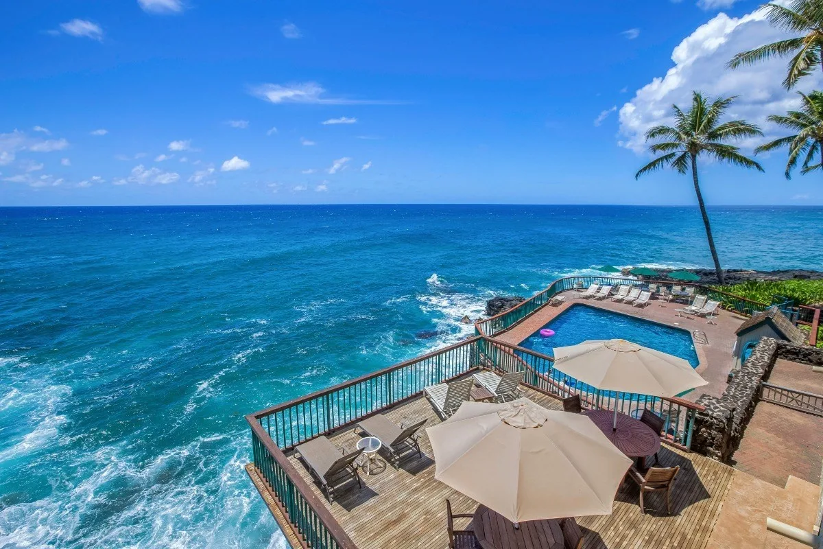 Una terraza con piscina frente al mar ofrece vistas al agua turquesa bajo un cielo azul.
