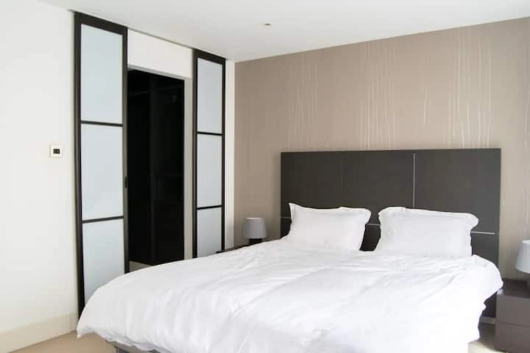 A bedroom with a bed, white bedding, and a dark headboard.