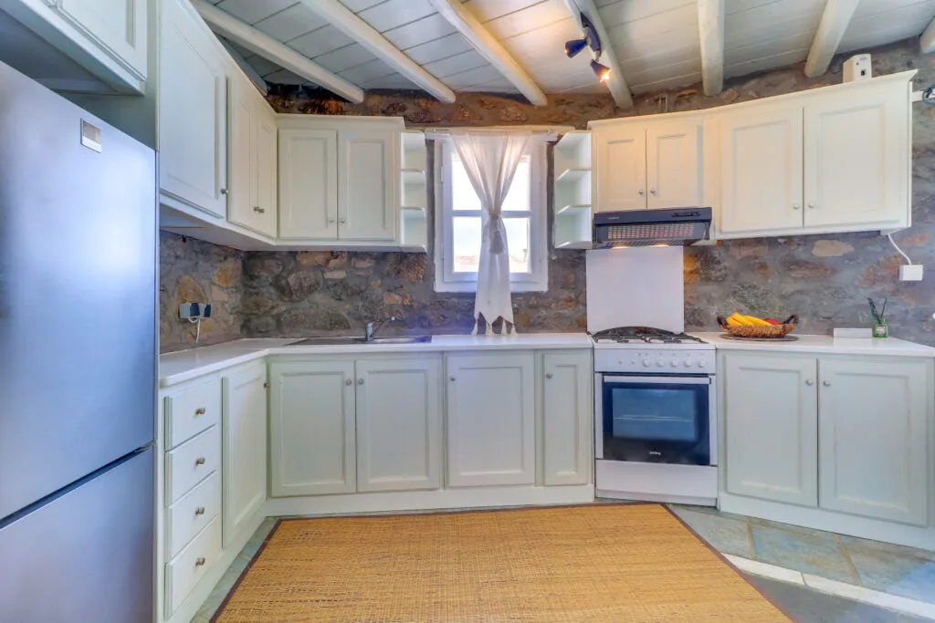 A bright kitchen with white cabinets, a stone backsplash, and a central window.