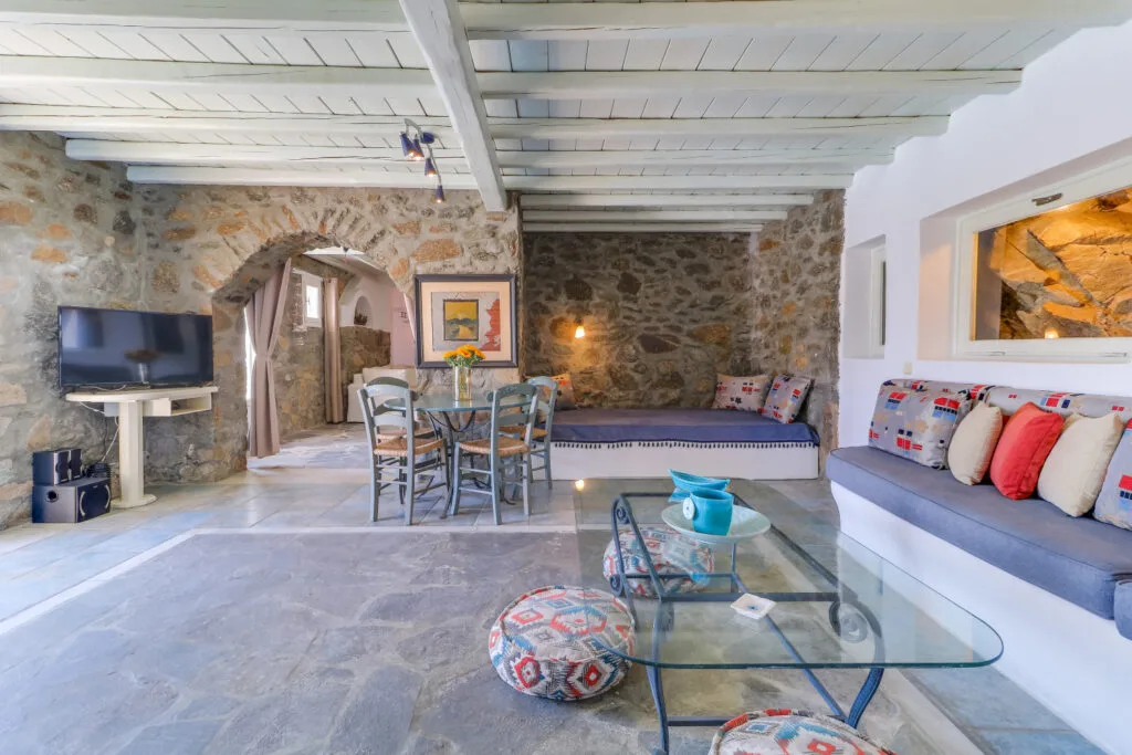 A stone-walled living room with seating, a dining table, and a television.