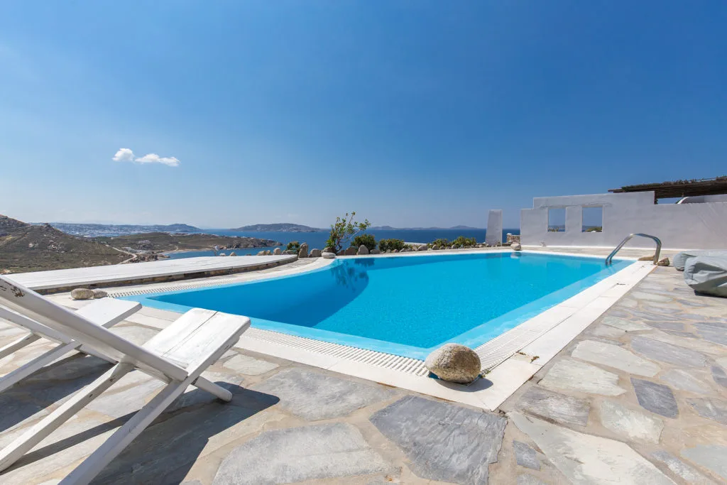 An outdoor swimming pool overlooks the sea, with loungers on the stone patio.