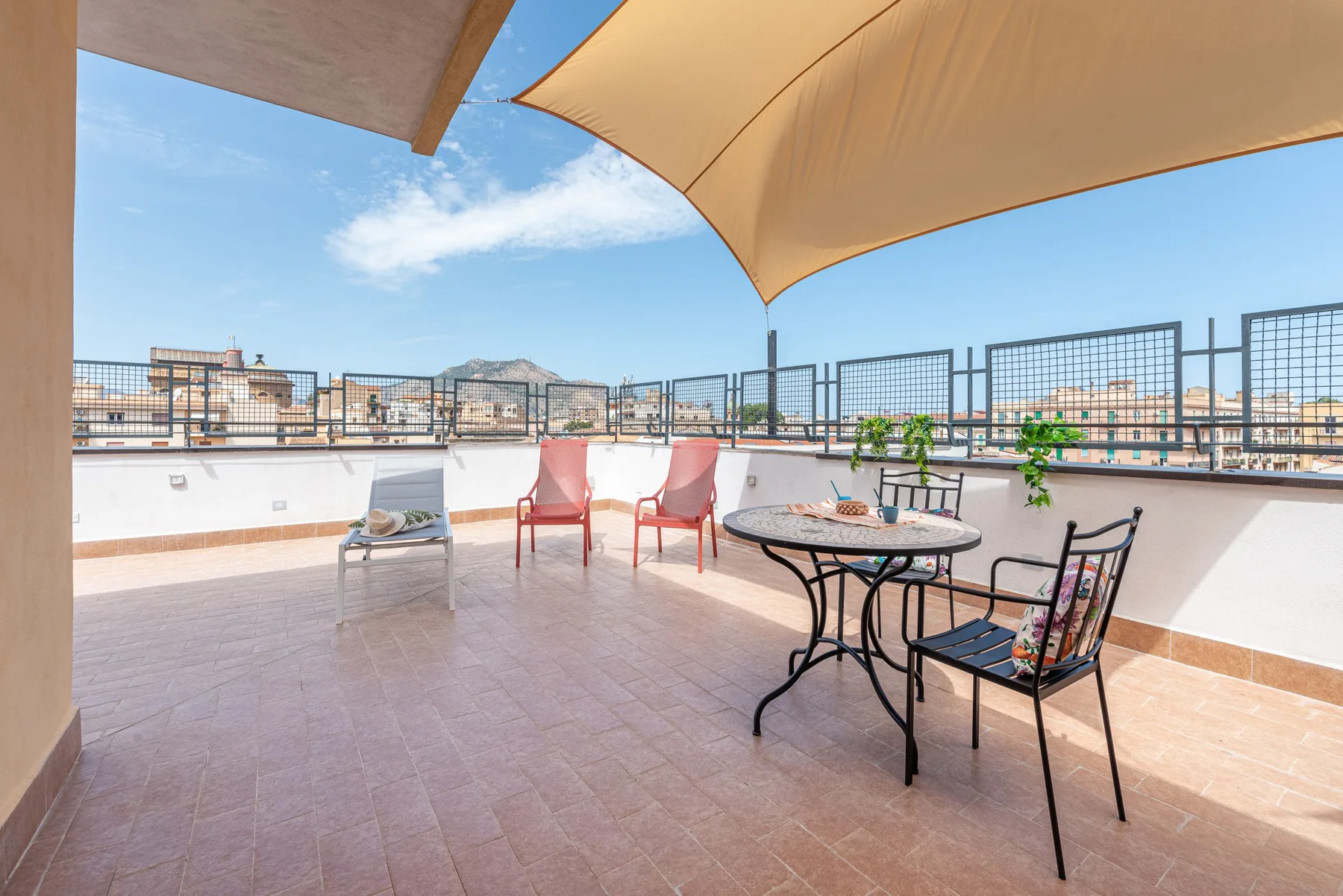 A sunny rooftop terrace with outdoor seating beneath a shade sail.