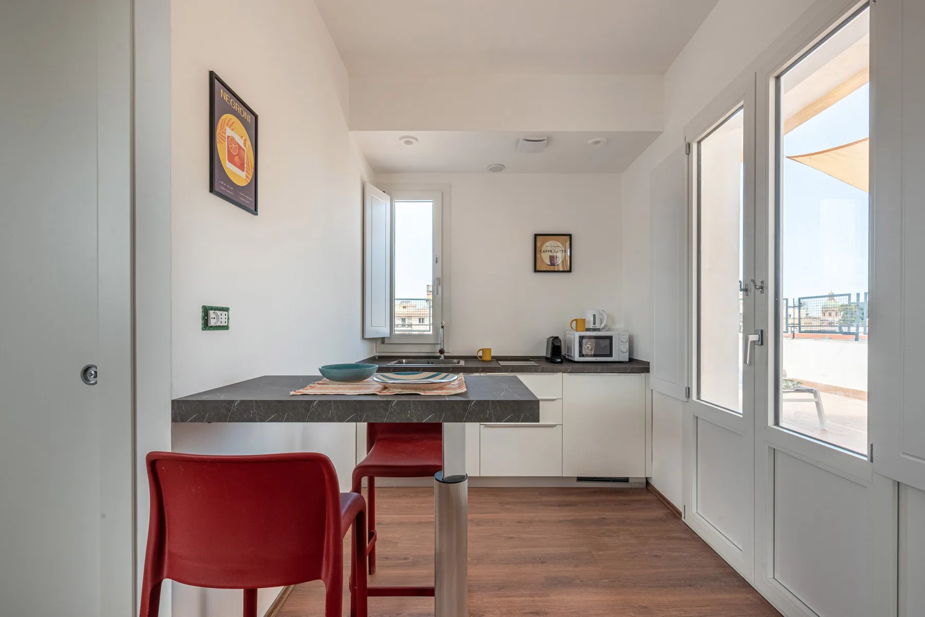 A bright kitchen and dining area with a counter, red seating, and glass doors.