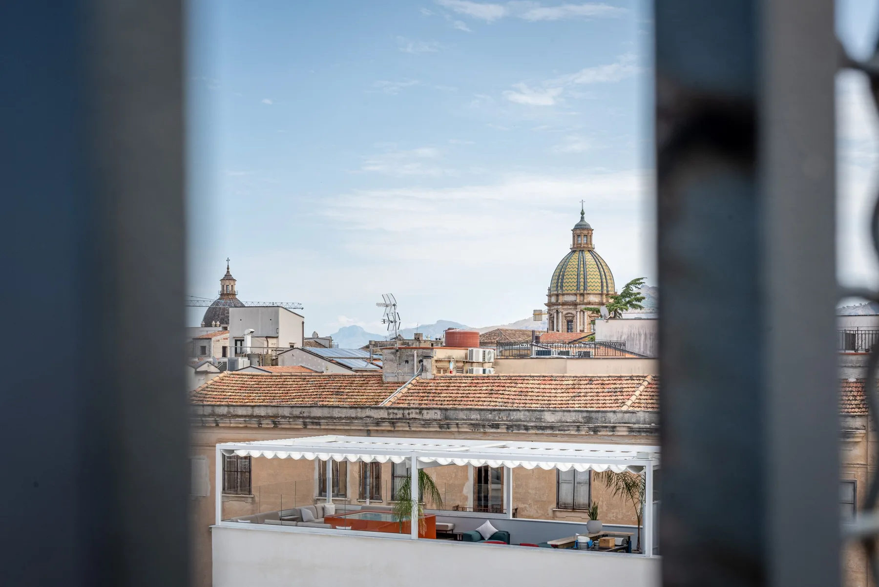 A city rooftop terrace overlooks tiled roofs and a domed church.