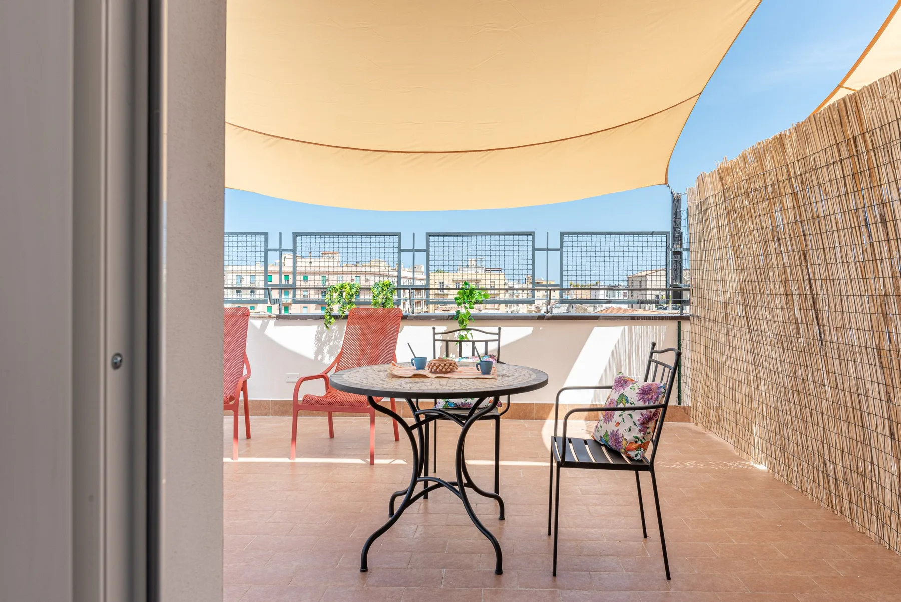 A furnished outdoor terrace with a round table, seating, and a fabric canopy.